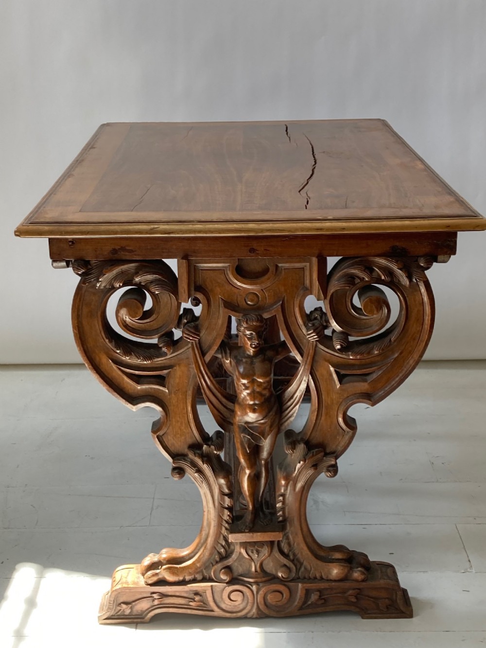 A 19th-century carved walnut library table featuring intricate trestle end supports with carved figurative male terms and scrolled foliage.