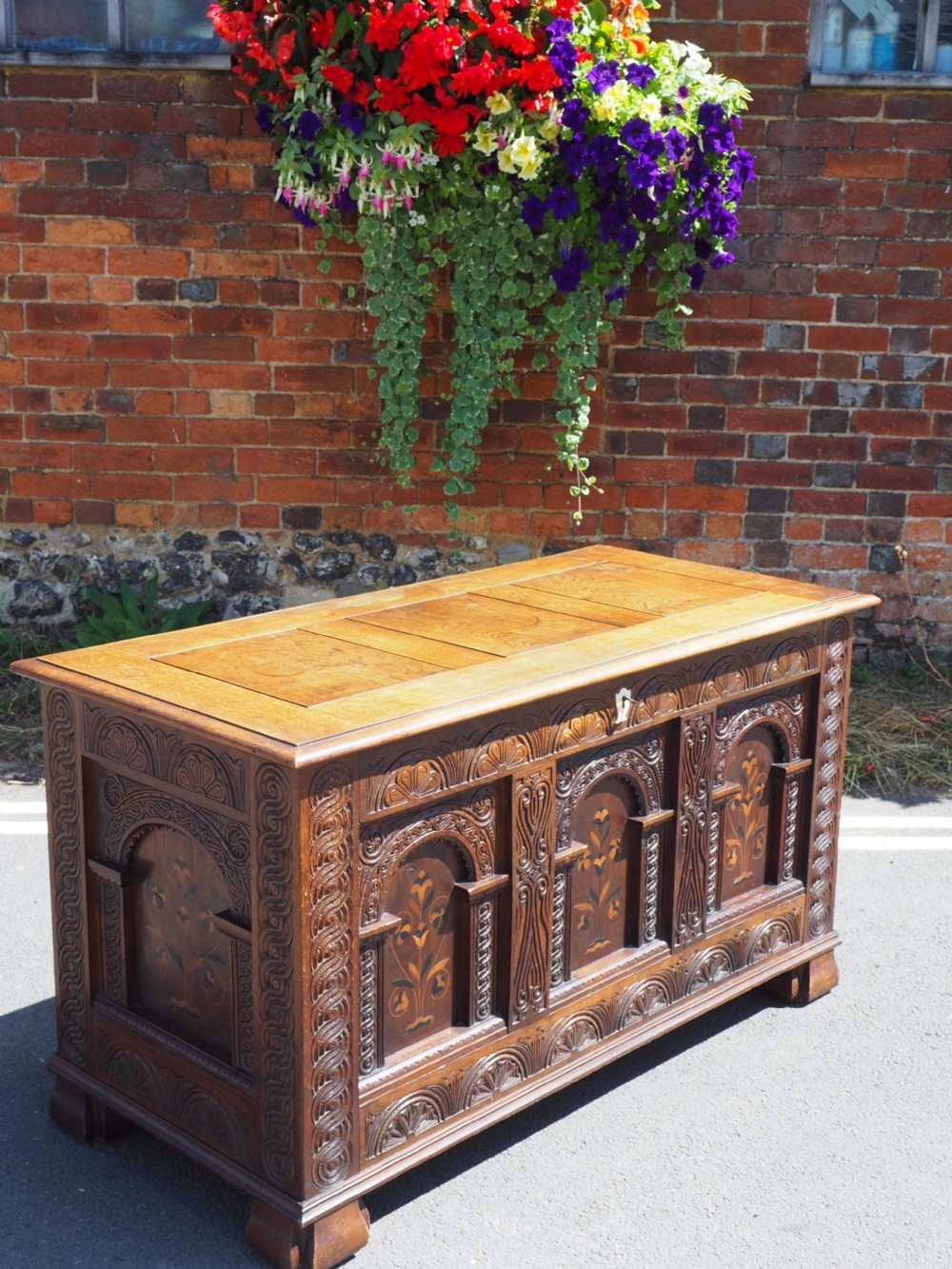A rectangular carved oak coffer with three arcaded front panels featuring floral inlay and a flat panelled top.