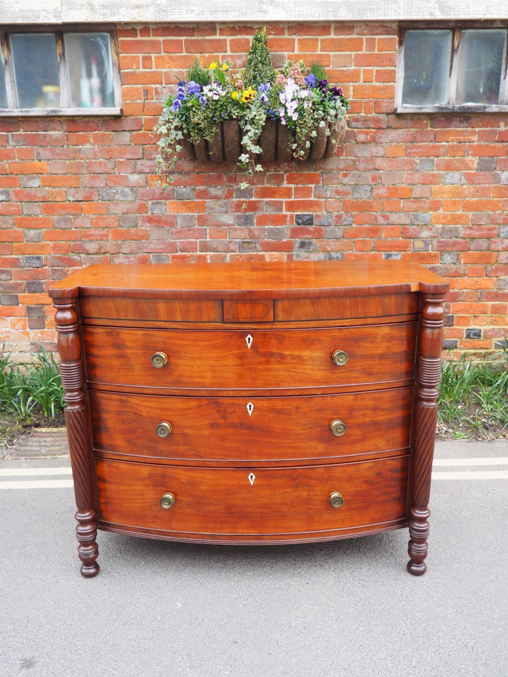 A Regency period mahogany bowfront chest of drawers featuring three full-width drawers, spiral-turned side columns, and circular brass handles.