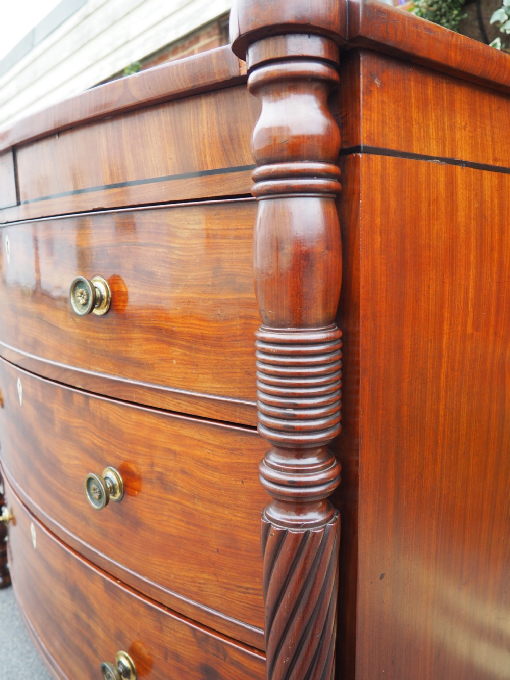 A Regency period mahogany bowfront chest of drawers featuring three full-width drawers, spiral-turned side columns, and circular brass handles. View VI