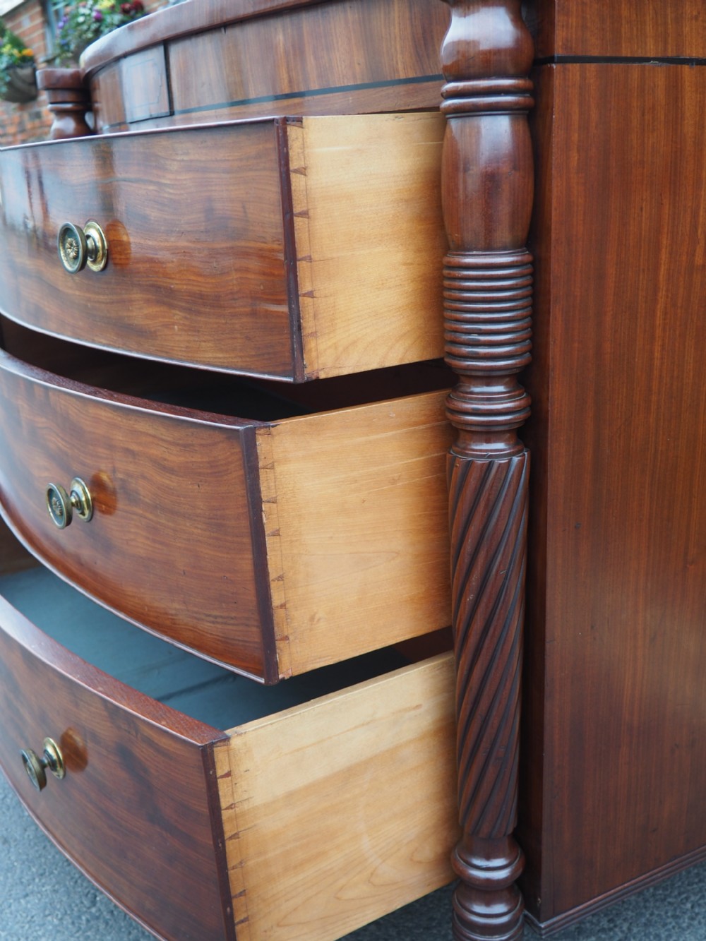 A Regency period mahogany bowfront chest of drawers featuring three full-width drawers, spiral-turned side columns, and circular brass handles. View VII