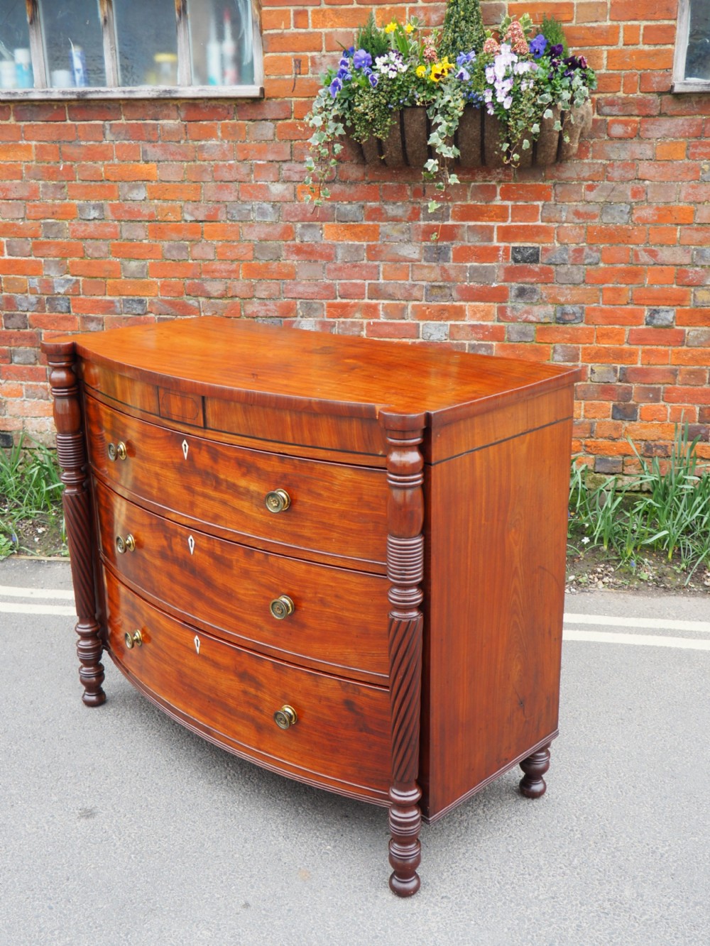 A Regency period mahogany bowfront chest of drawers featuring three full-width drawers, spiral-turned side columns, and circular brass handles. View XI