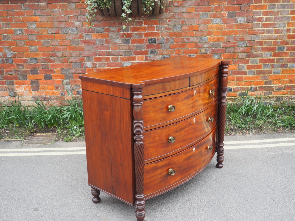 A Regency period mahogany bowfront chest of drawers featuring three full-width drawers, spiral-turned side columns, and circular brass handles. View XIV