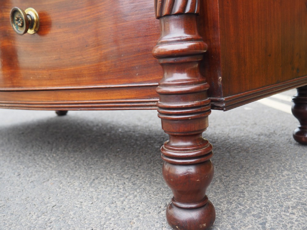 A Regency period mahogany bowfront chest of drawers featuring three full-width drawers, spiral-turned side columns, and circular brass handles. View XVI