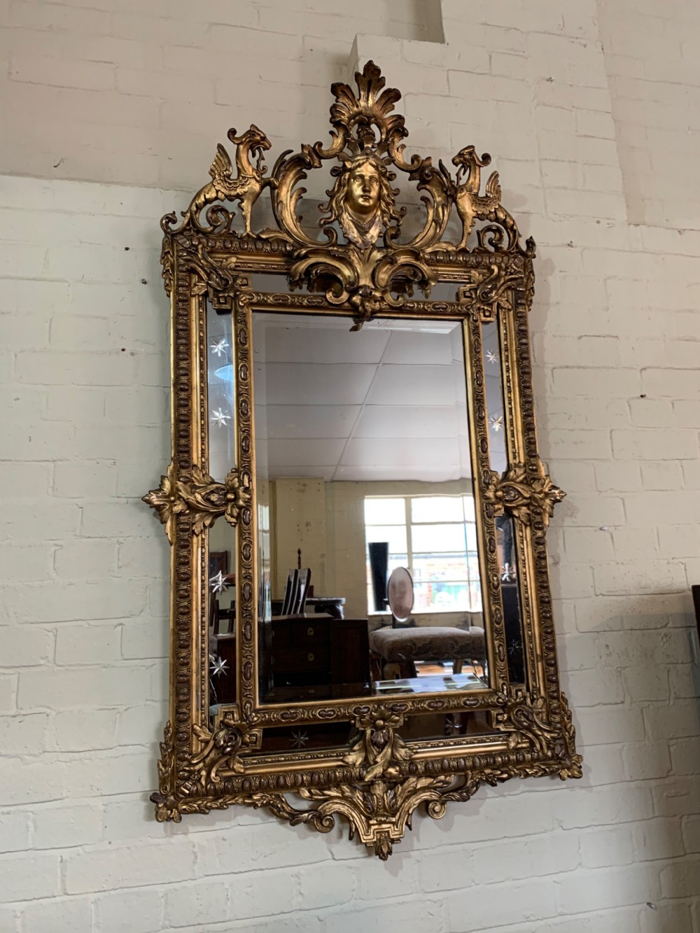 A nineteenth-century rectangular giltwood wall mirror featuring a carved crest with a sculpted mask, winged creatures, and star-etched border panels.
