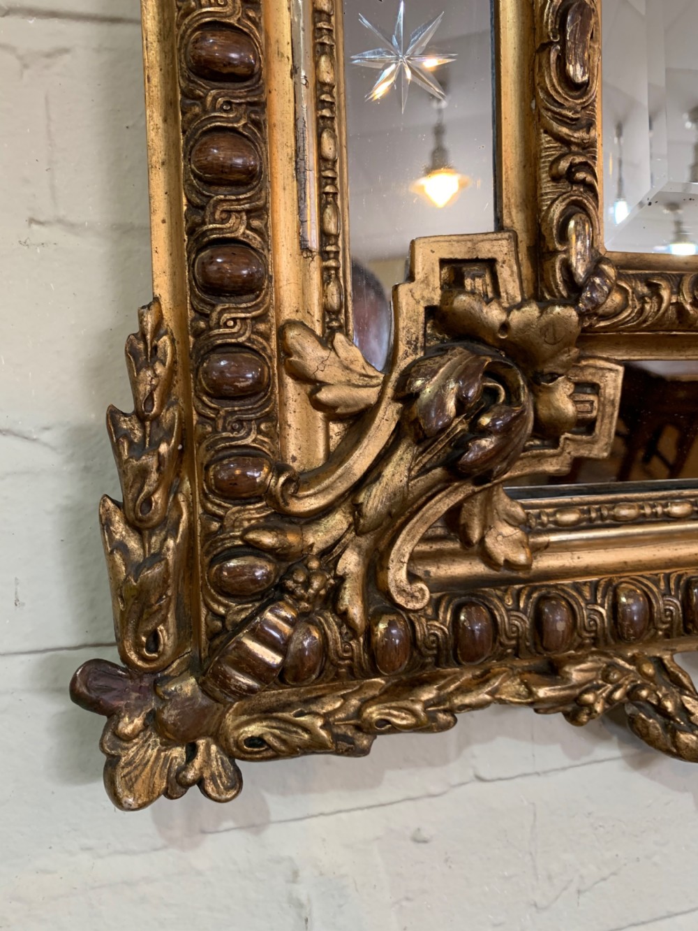 A nineteenth-century rectangular giltwood wall mirror featuring a carved crest with a sculpted mask, winged creatures, and star-etched border panels. View II