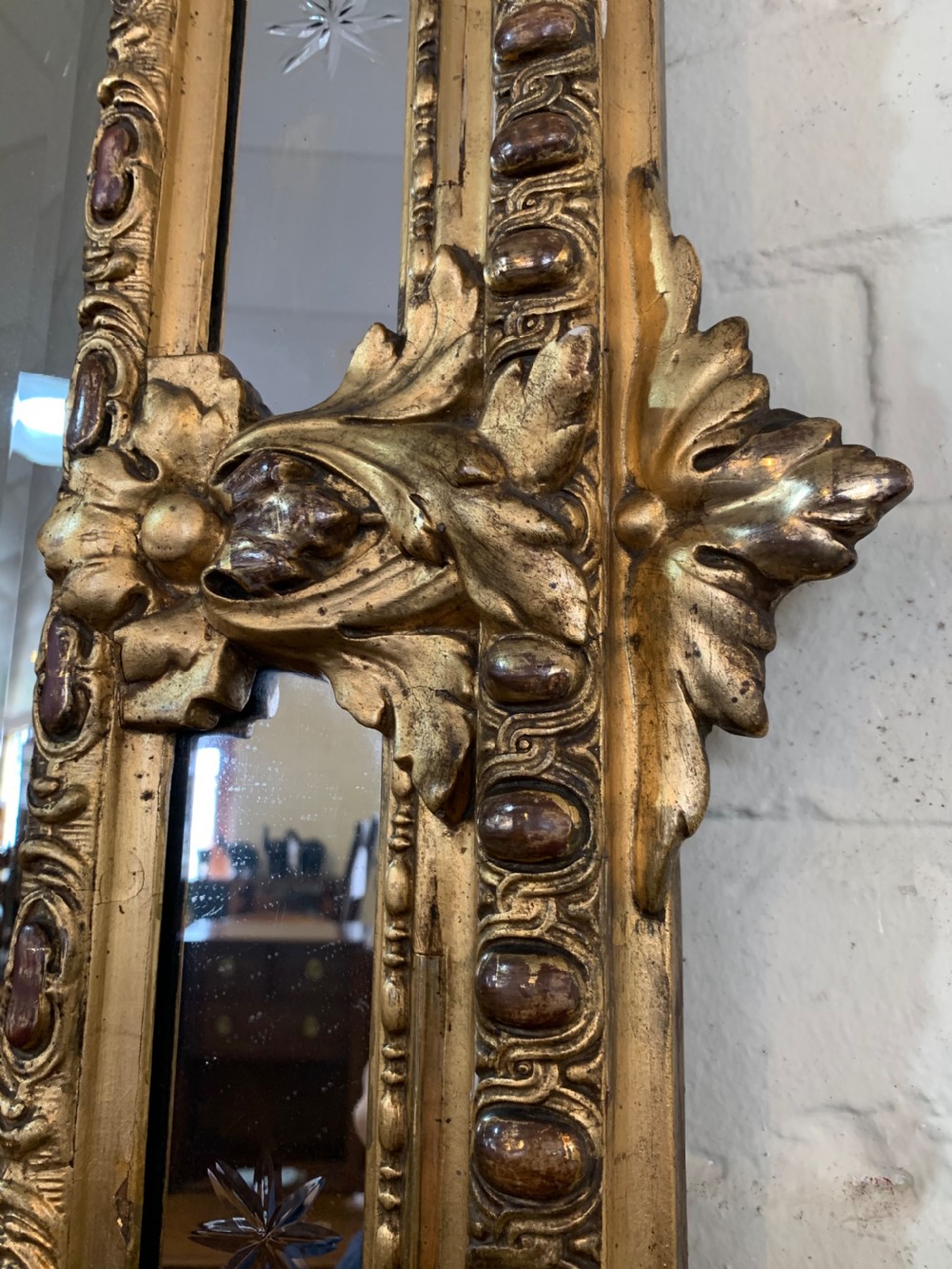 A nineteenth-century rectangular giltwood wall mirror featuring a carved crest with a sculpted mask, winged creatures, and star-etched border panels. View V