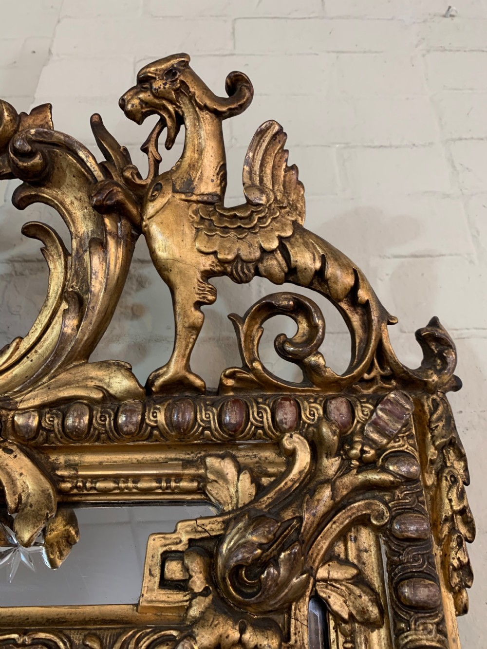 A nineteenth-century rectangular giltwood wall mirror featuring a carved crest with a sculpted mask, winged creatures, and star-etched border panels. View VIII