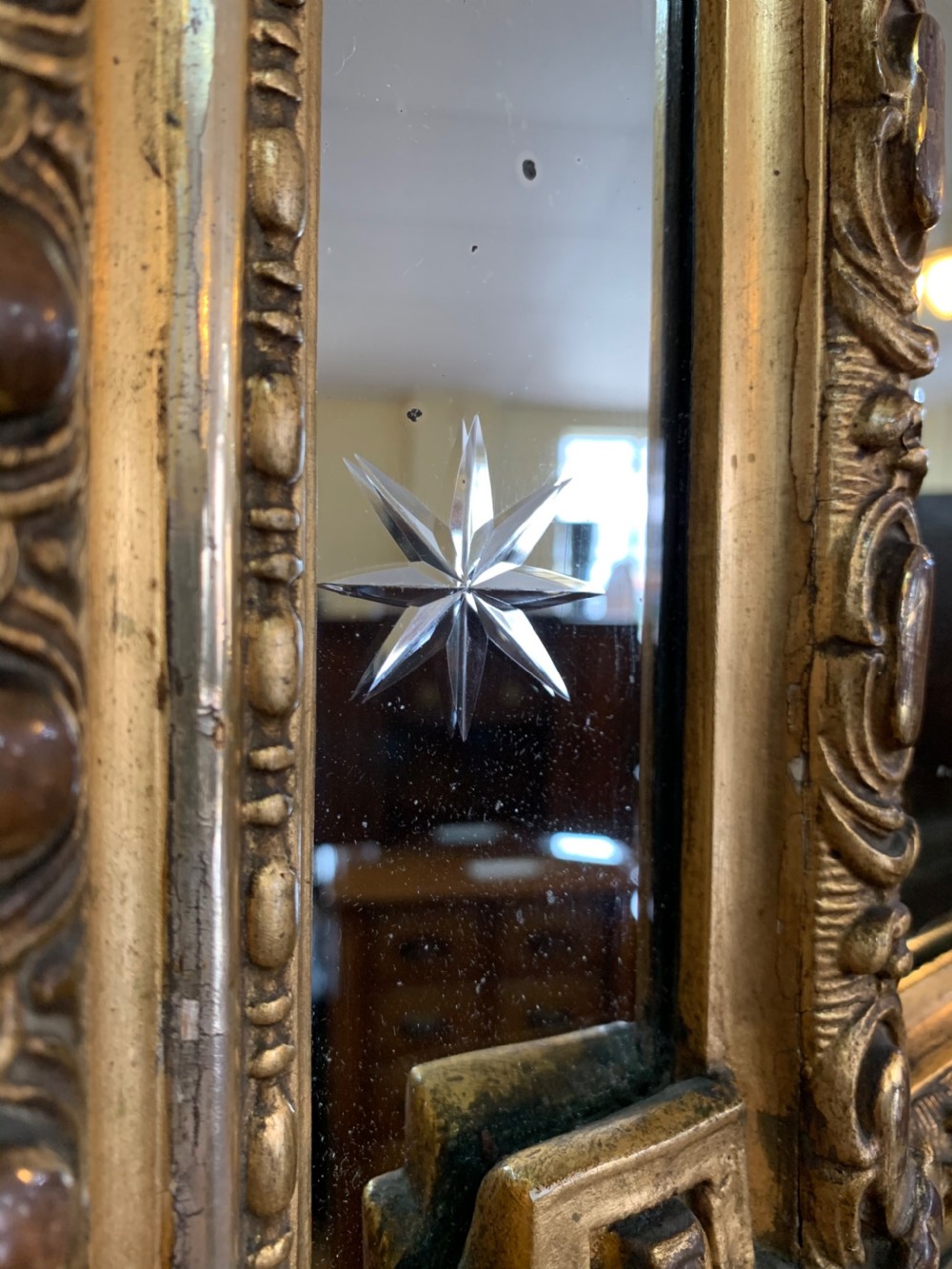 A nineteenth-century rectangular giltwood wall mirror featuring a carved crest with a sculpted mask, winged creatures, and star-etched border panels. View IX