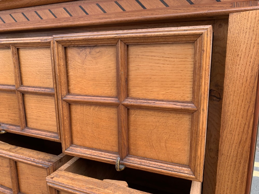 A low three-door oak vestry cupboard featuring clear glass panels, incised frieze carving, and bun feet. View IX