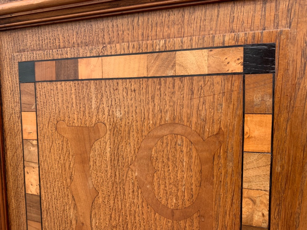 A low three-door oak vestry cupboard featuring clear glass panels, incised frieze carving, and bun feet. View XII