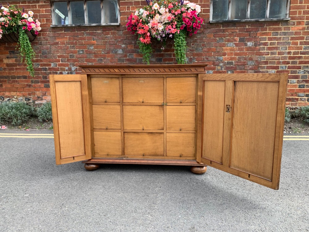 A low three-door oak vestry cupboard featuring clear glass panels, incised frieze carving, and bun feet. View XIII