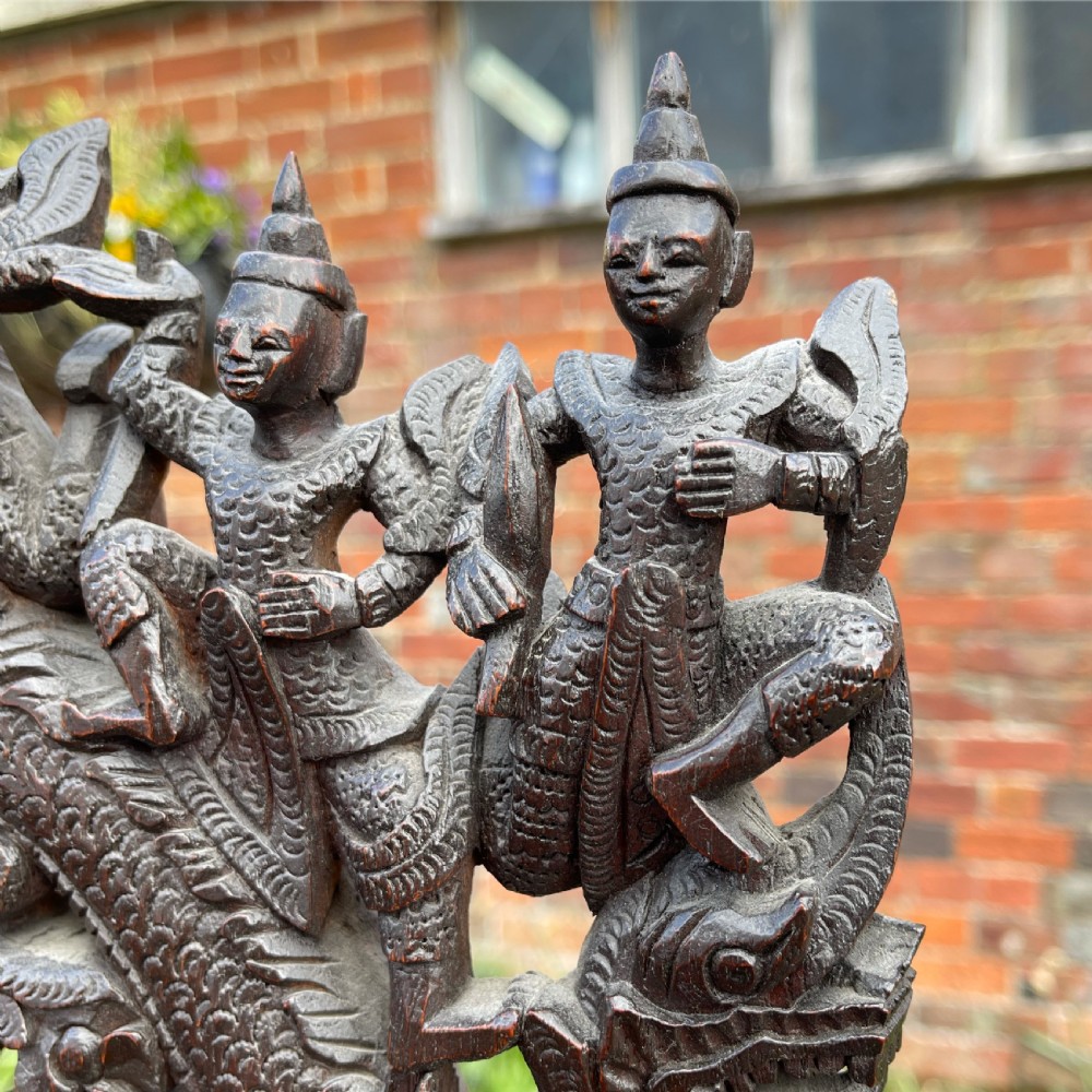 A three-tier dark teak carved whatnot featuring spiralled support posts and a deeply carved mythological cresting gallery at the top. View V