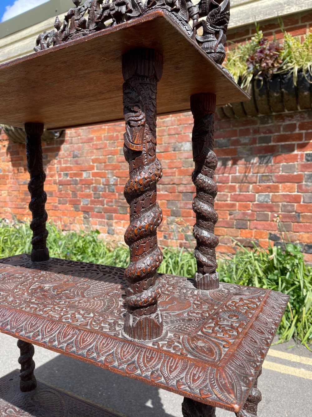 A three-tier dark teak carved whatnot featuring spiralled support posts and a deeply carved mythological cresting gallery at the top. View VIII