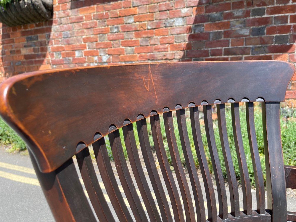 A dark brown wood revolving desk chair featuring a curved slatted backrest, turned arm posts, a contoured seat, and four splayed legs with brass castors. View V
