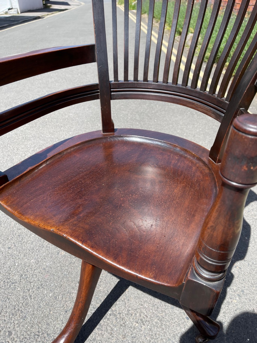 A dark brown wood revolving desk chair featuring a curved slatted backrest, turned arm posts, a contoured seat, and four splayed legs with brass castors. View VII