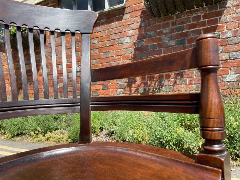 A dark brown wood revolving desk chair featuring a curved slatted backrest, turned arm posts, a contoured seat, and four splayed legs with brass castors. View IX