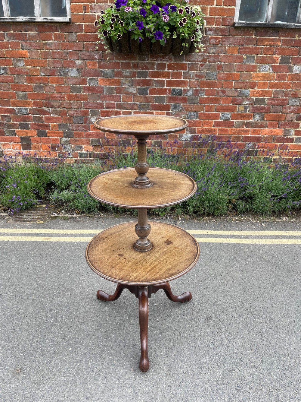 A George III mahogany three-tier dumb waiter featuring graduated circular trays supported by turned stem sections and a tripod base with pad feet.