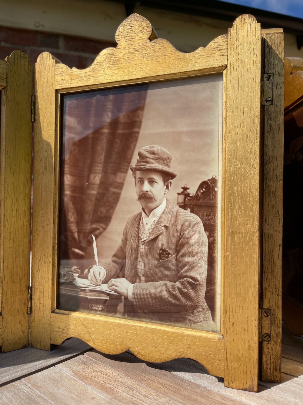 An Edwardian six-fold giltwood photo frame featuring shaped top crests and monochrome portrait photographs. View VI