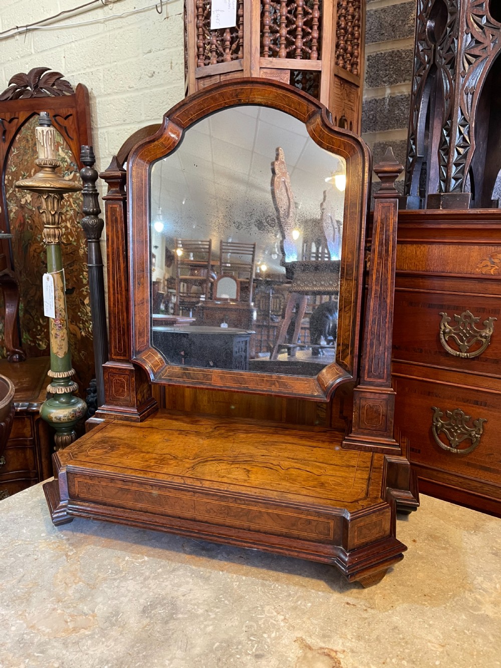An antique burr walnut dressing mirror featuring an arched frame, crossbanded inlay, supporting upright posts with finials, and a stepped plinth base.