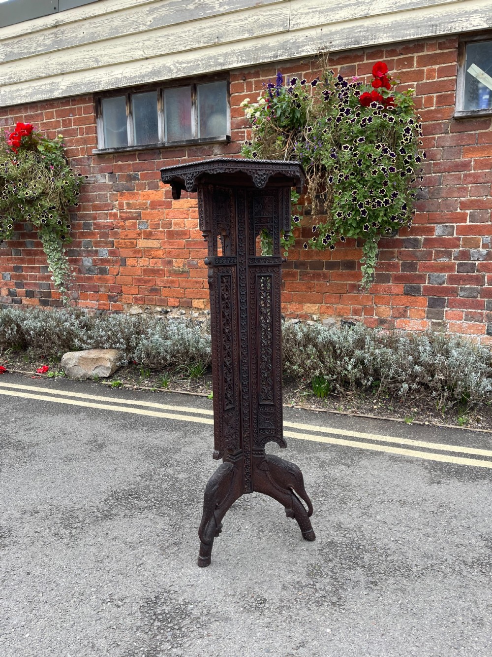 A tall, dark carved hardwood Anglo-Indian pedestal stand featuring intricate pierced fretwork along the column and carved elephant heads forming the base legs.