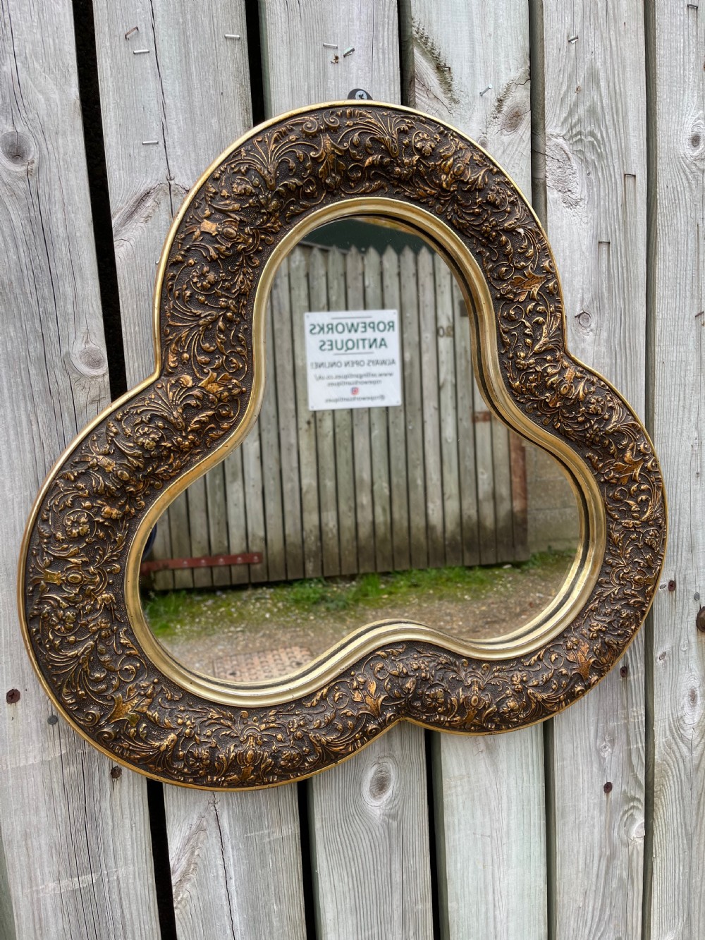 A nineteenth-century shaped gilt mirror featuring an ornate foliate relief border and a trefoil contour.
