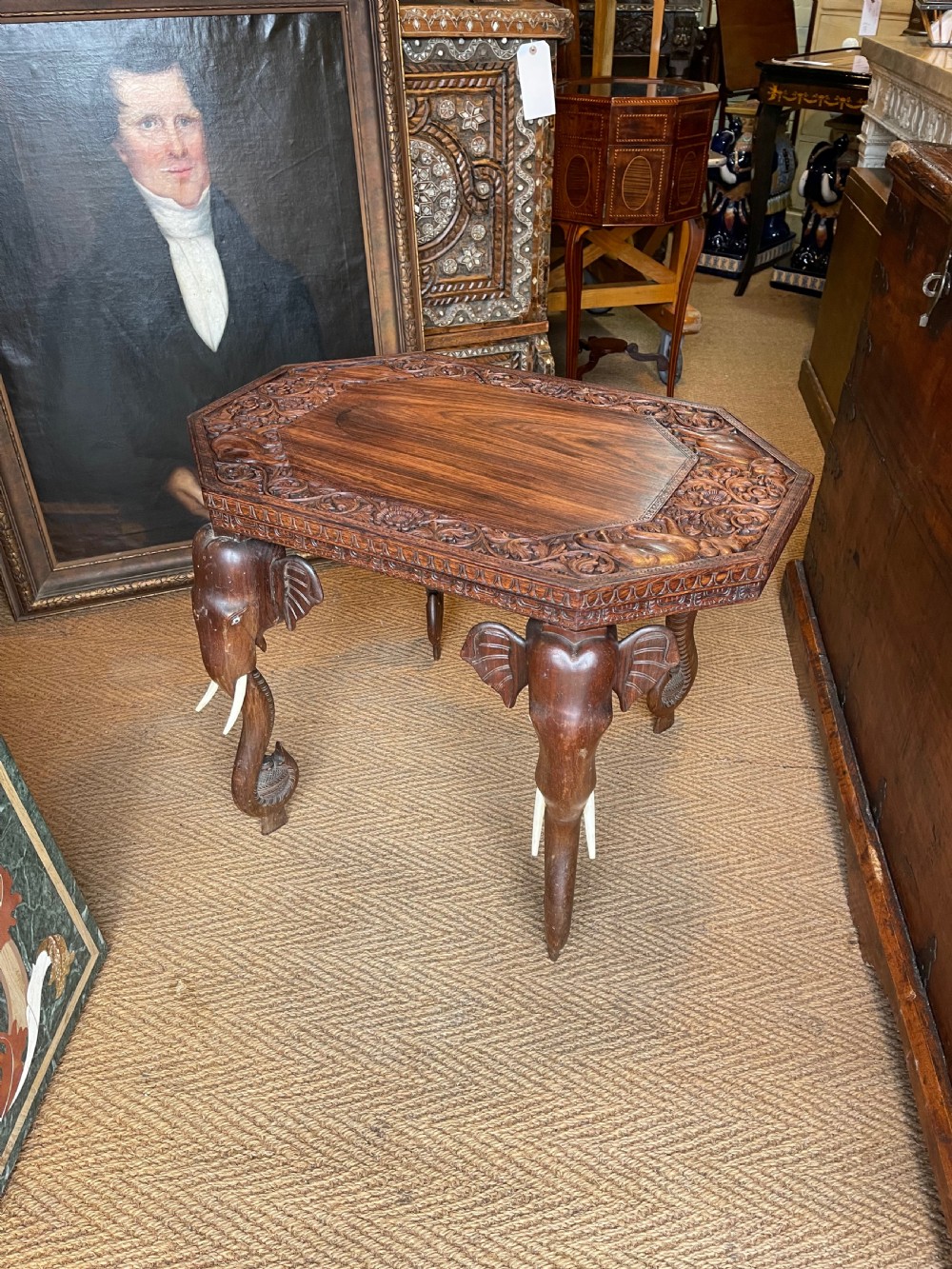 A hand-carved dark wood octagonal side table featuring carved elephant head legs with bone tusks and a floral border.