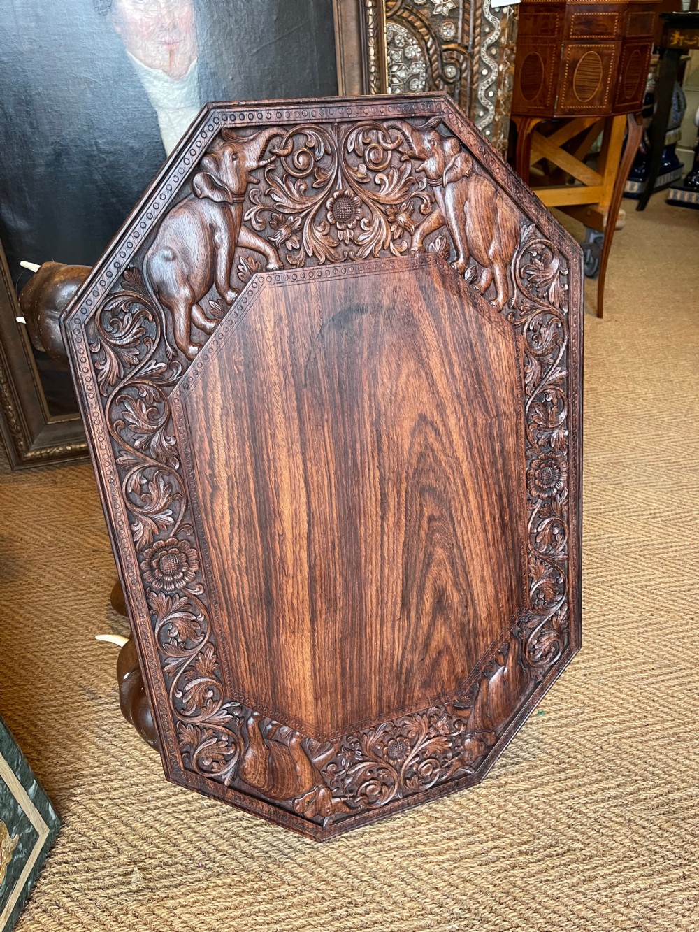 A hand-carved dark wood octagonal side table featuring carved elephant head legs with bone tusks and a floral border. View II