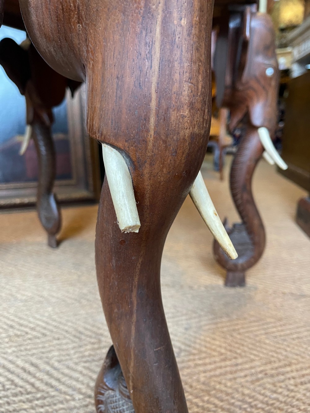 A hand-carved dark wood octagonal side table featuring carved elephant head legs with bone tusks and a floral border. View III