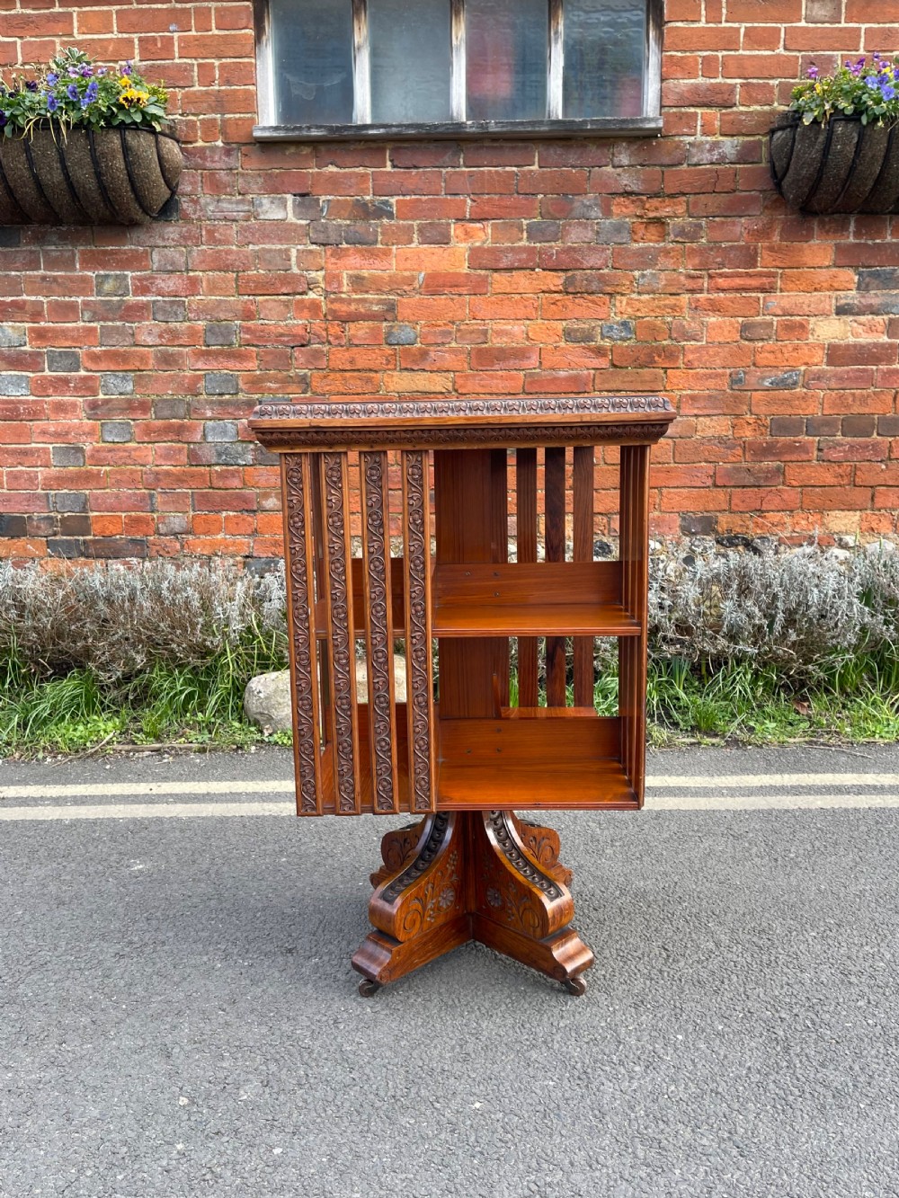An Anglo-Indian carved wood revolving bookcase featuring vertical foliate slats and a tiered pedestal base.