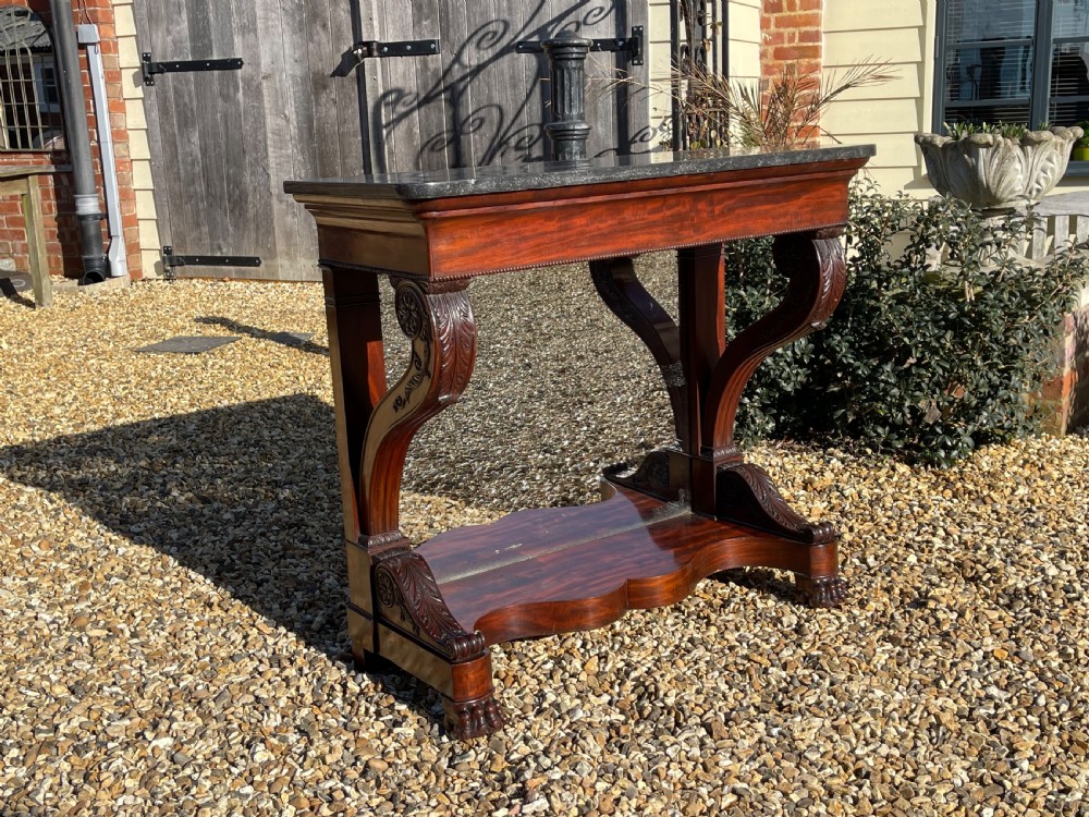 A nineteenth-century French mahogany console table featuring a dark marble top, carved S-scroll legs, and an undertier shelf on claw feet.