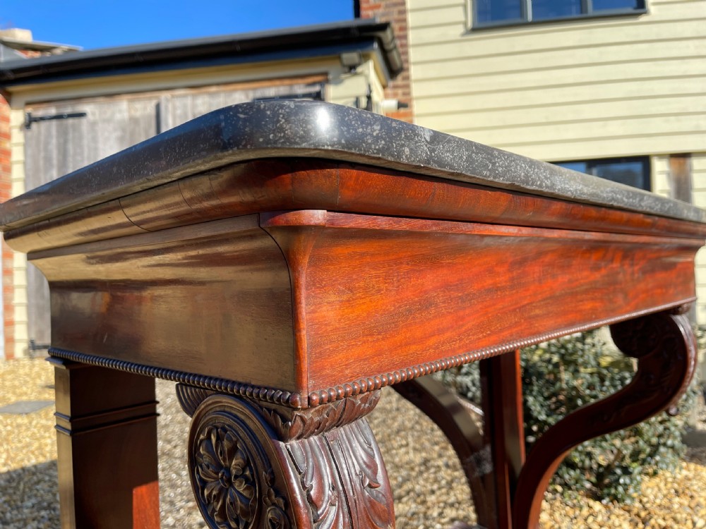 A nineteenth-century French mahogany console table featuring a dark marble top, carved S-scroll legs, and an undertier shelf on claw feet. View III
