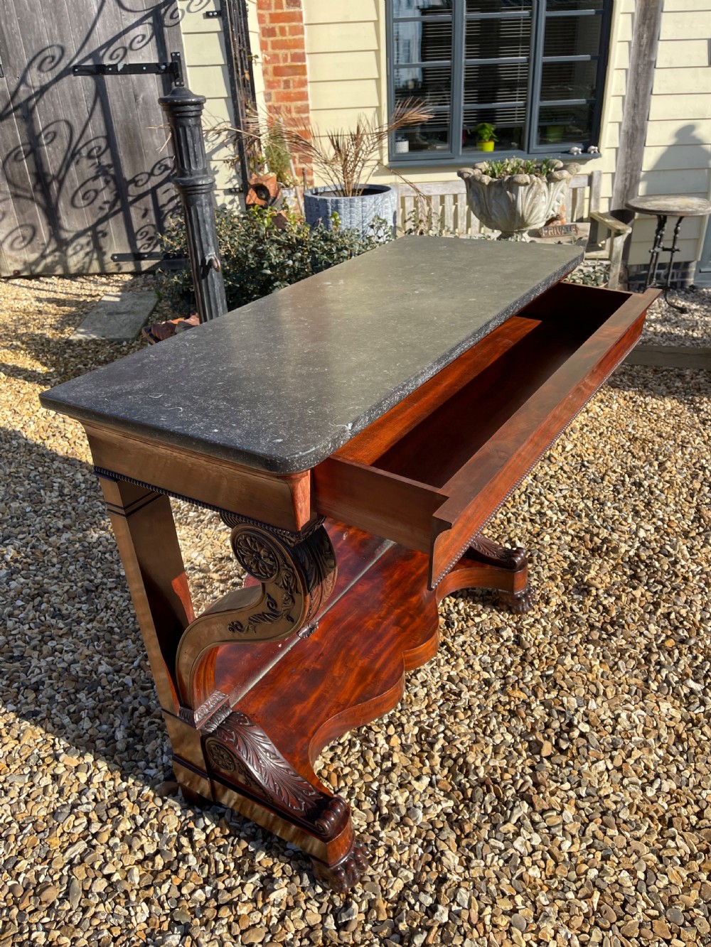A nineteenth-century French mahogany console table featuring a dark marble top, carved S-scroll legs, and an undertier shelf on claw feet. View V