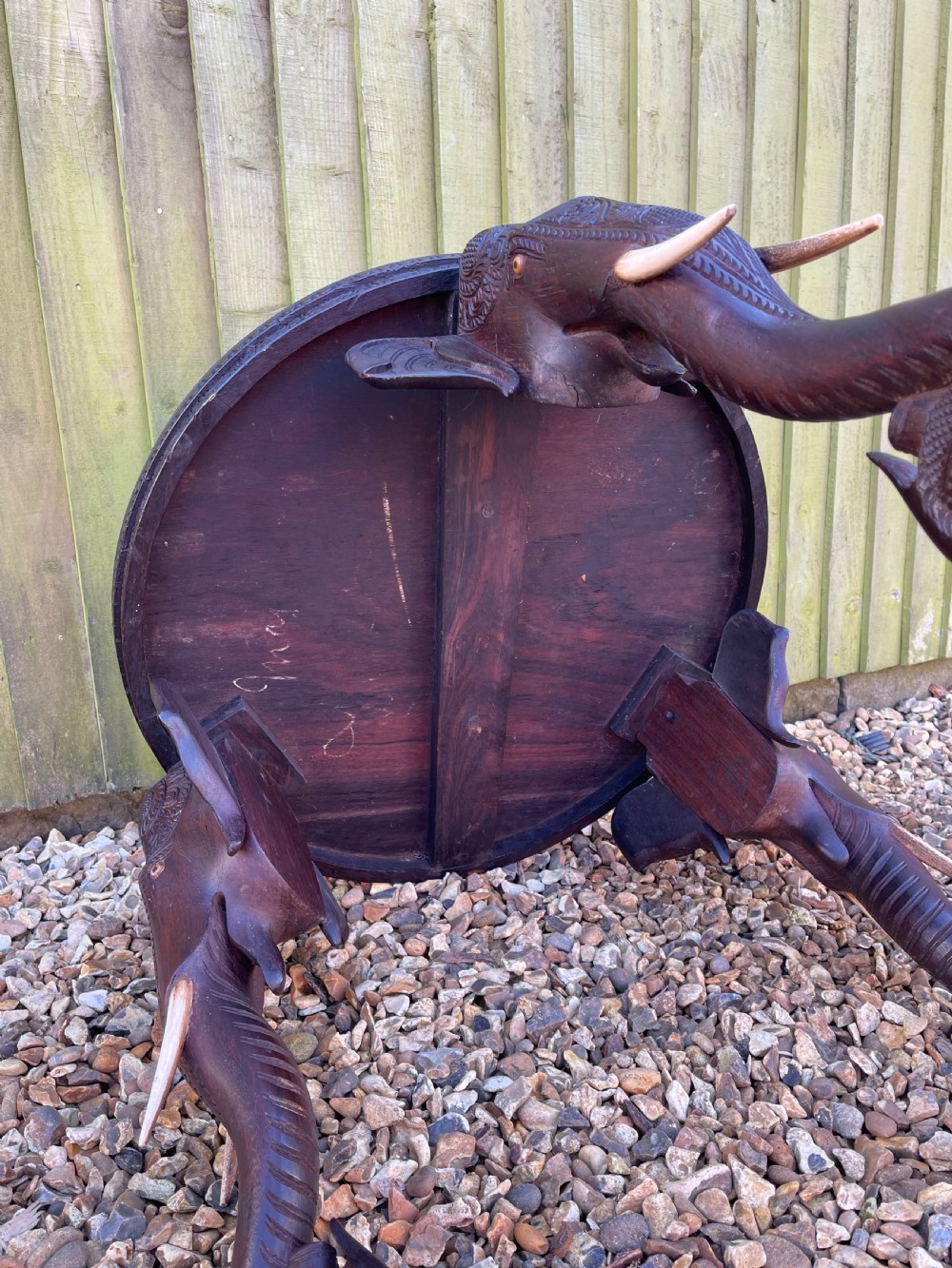 A circular dark wood carved side table with three legs shaped like elephant heads and trunks with bone tusks. View IV