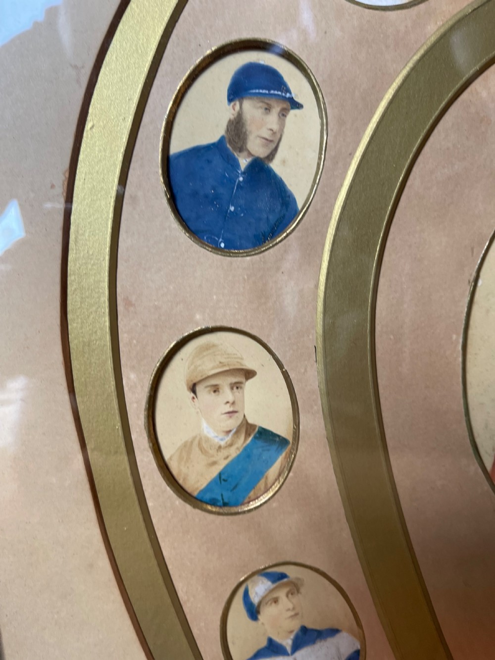 A pair of dark wood framed prints displaying miniature jockey portraits arranged inside gilded horseshoe-shaped matting. View II