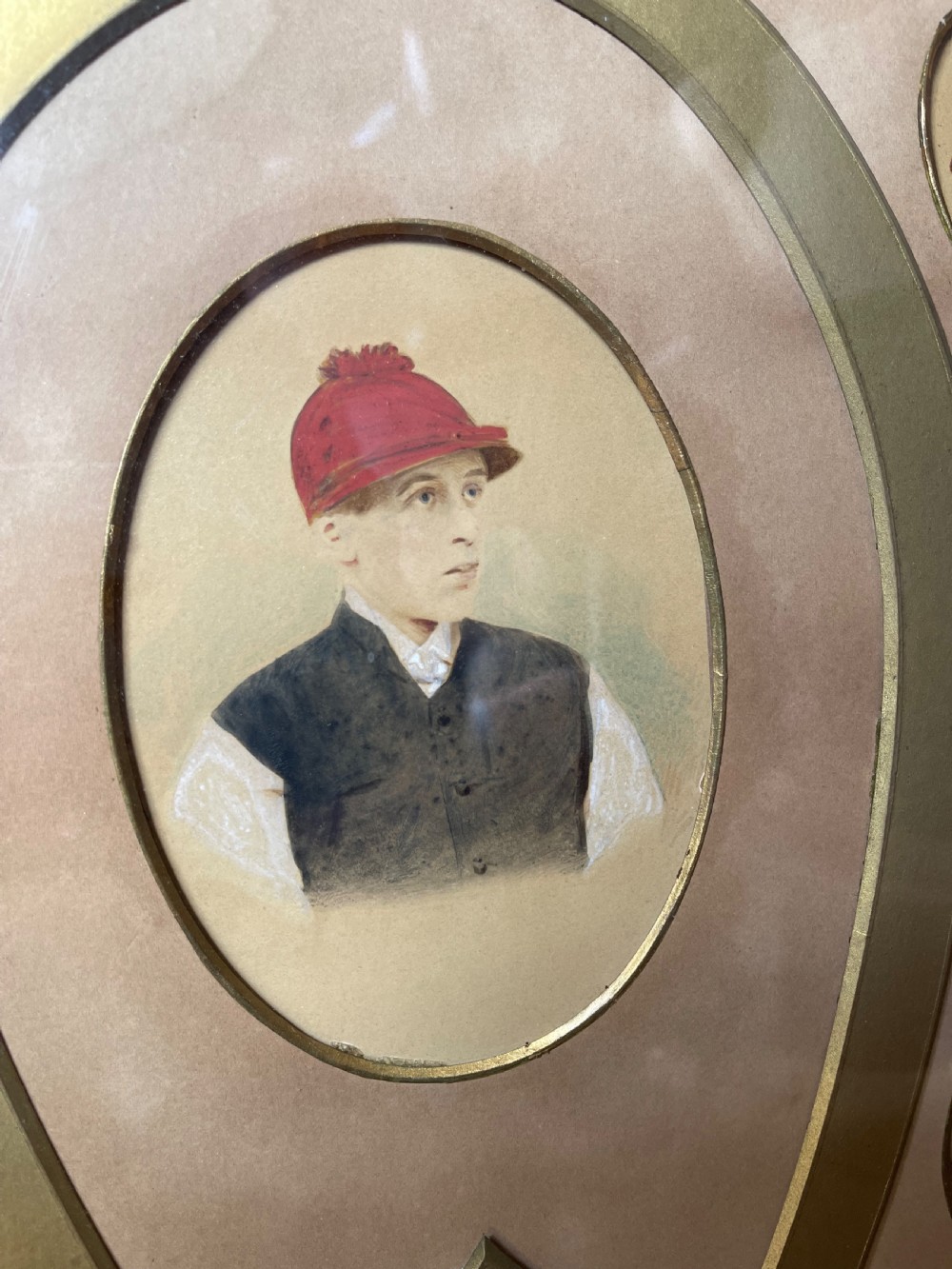A pair of dark wood framed prints displaying miniature jockey portraits arranged inside gilded horseshoe-shaped matting. View V