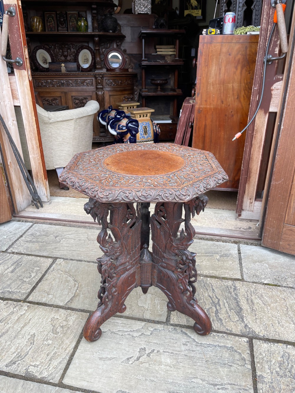 A nineteenth-century octagonal Burmese teak side table featuring intricately carved floral borders and openwork carved legs with mythical animal motifs.