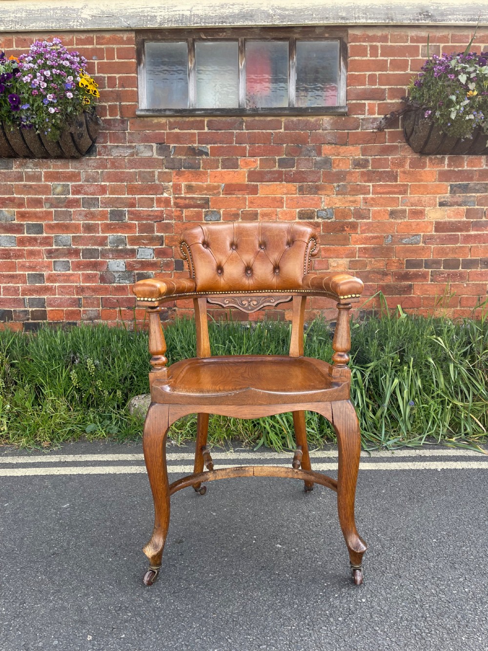 A Victorian oak desk chair featuring a deep-buttoned brown leather horseshoe backrest, turned arm supports, a shaped oak seat, and front cabriole legs on brass castors.