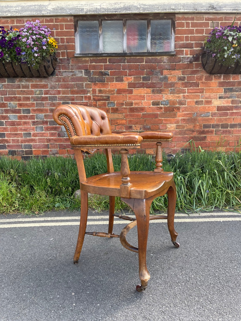 A Victorian oak desk chair featuring a deep-buttoned brown leather horseshoe backrest, turned arm supports, a shaped oak seat, and front cabriole legs on brass castors. View II