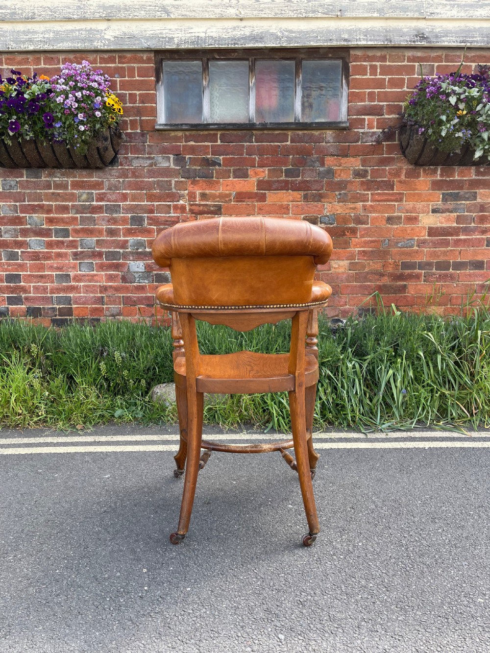 A Victorian oak desk chair featuring a deep-buttoned brown leather horseshoe backrest, turned arm supports, a shaped oak seat, and front cabriole legs on brass castors. View III