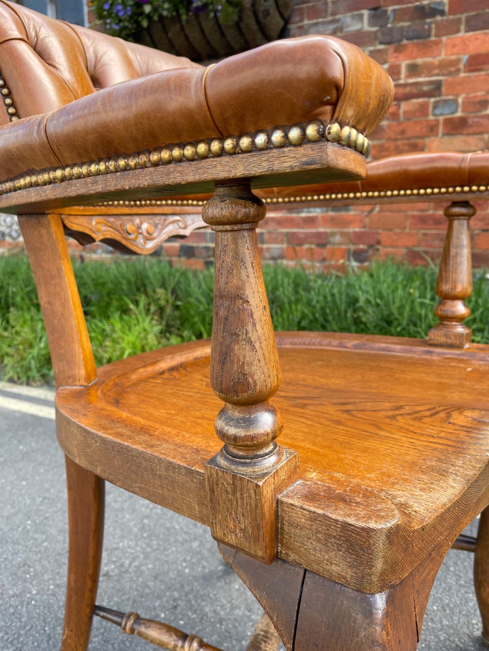 A Victorian oak desk chair featuring a deep-buttoned brown leather horseshoe backrest, turned arm supports, a shaped oak seat, and front cabriole legs on brass castors. View VI