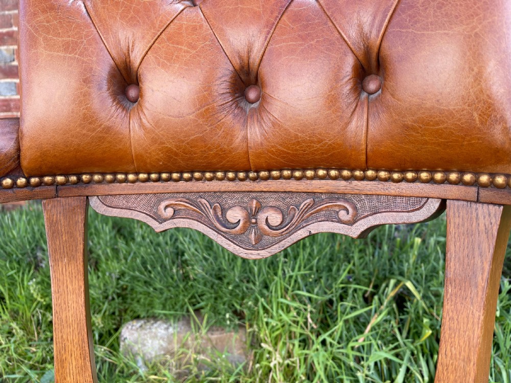 A Victorian oak desk chair featuring a deep-buttoned brown leather horseshoe backrest, turned arm supports, a shaped oak seat, and front cabriole legs on brass castors. View VII