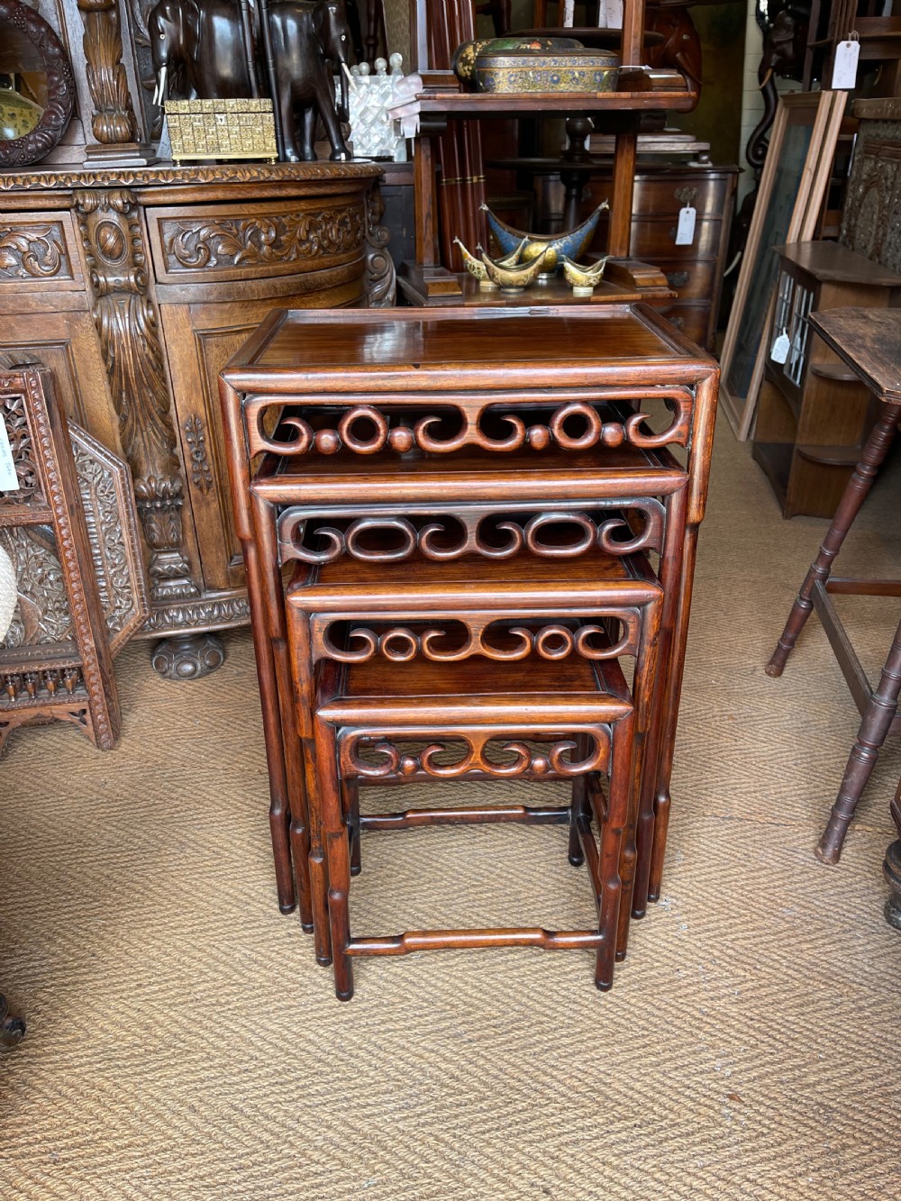 A set of four graduated dark hardwood nesting tables featuring pierced openwork aprons and bamboo-form carved legs.
