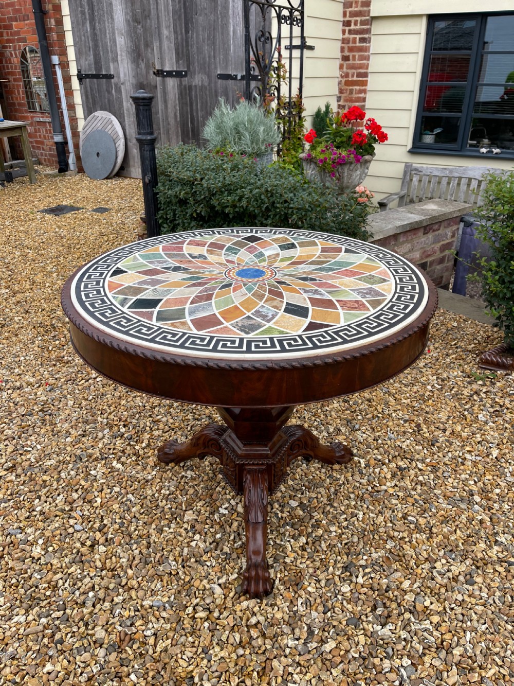 A circular nineteenth-century mahogany centre table featuring a geometric specimen marble mosaic top bordered by a Greek key pattern, supported by a carved pedestal base.