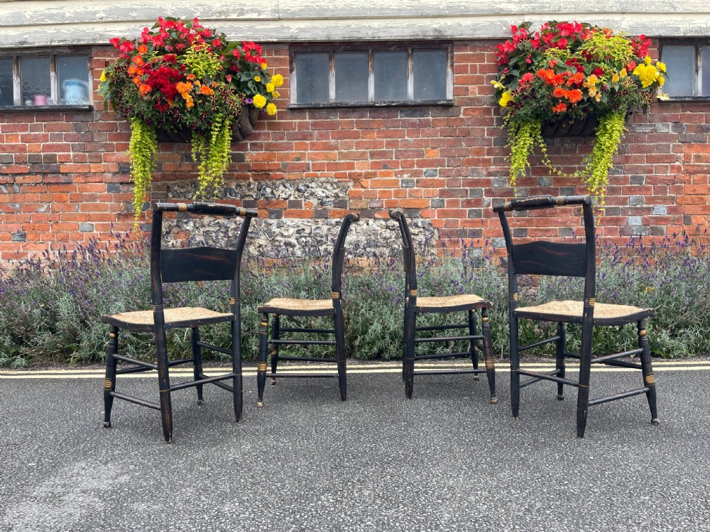 A set of four black-painted wooden side chairs featuring gold stencilled foliage, turned legs, horizontal back slats, and rush seats. View IV