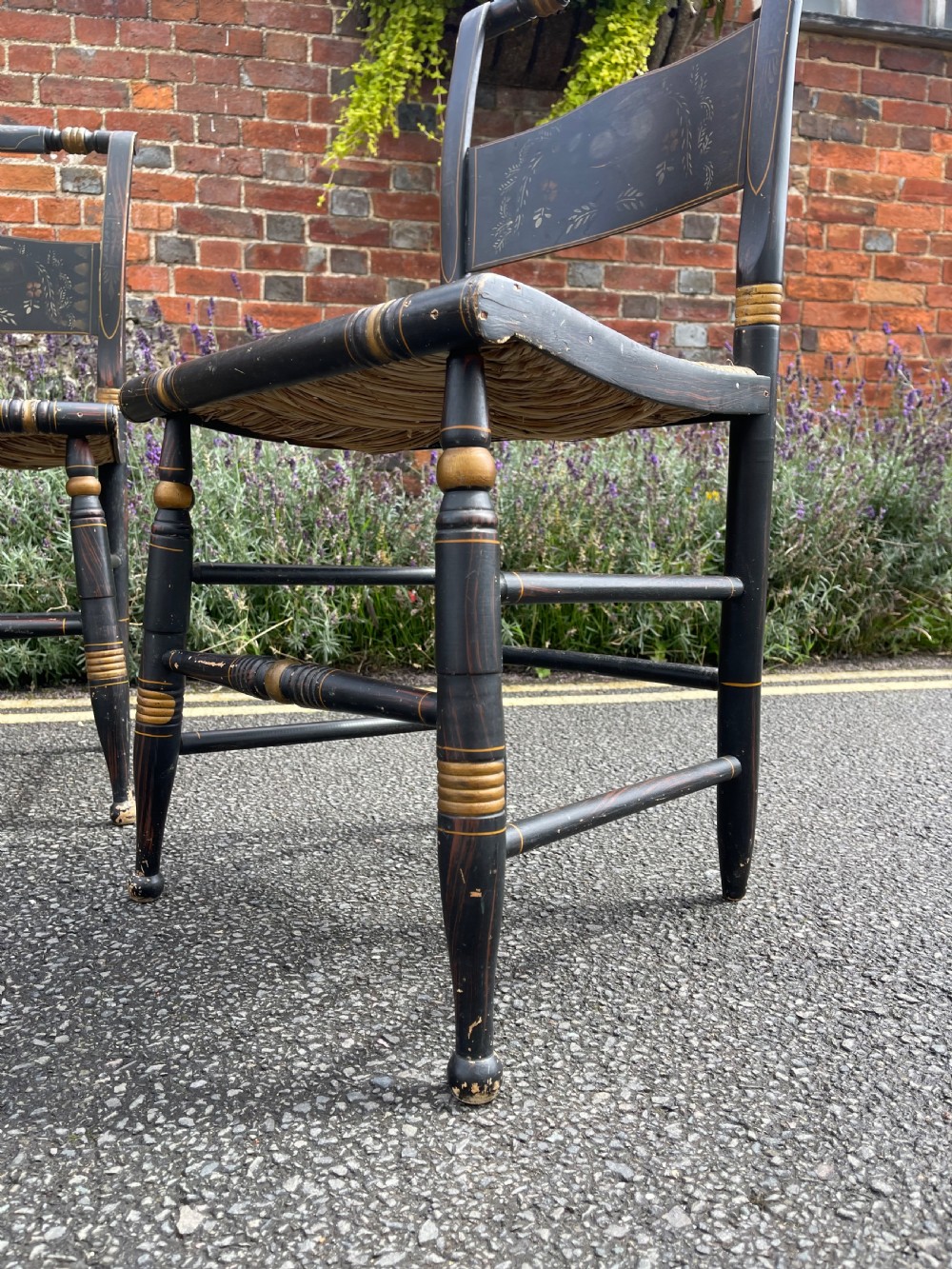 A set of four black-painted wooden side chairs featuring gold stencilled foliage, turned legs, horizontal back slats, and rush seats. View VI