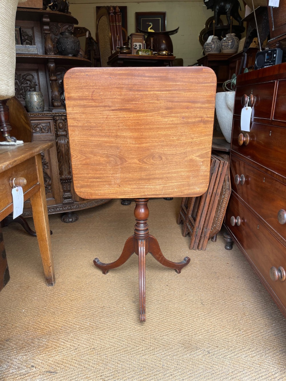 A Georgian mahogany tilt top table displayed vertically, featuring a rectangular top, turned central column, and reeded tripod legs.
