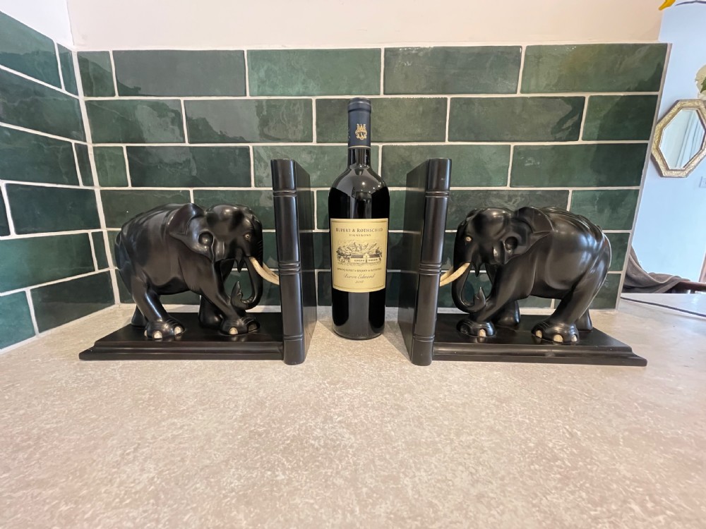A pair of dark carved wooden elephant bookends with bone tusks on rectangular bases.