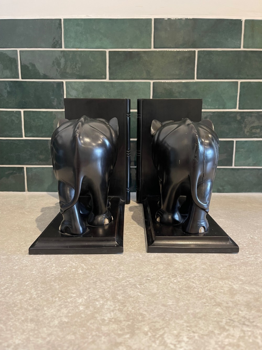 A pair of dark carved wooden elephant bookends with bone tusks on rectangular bases. View II