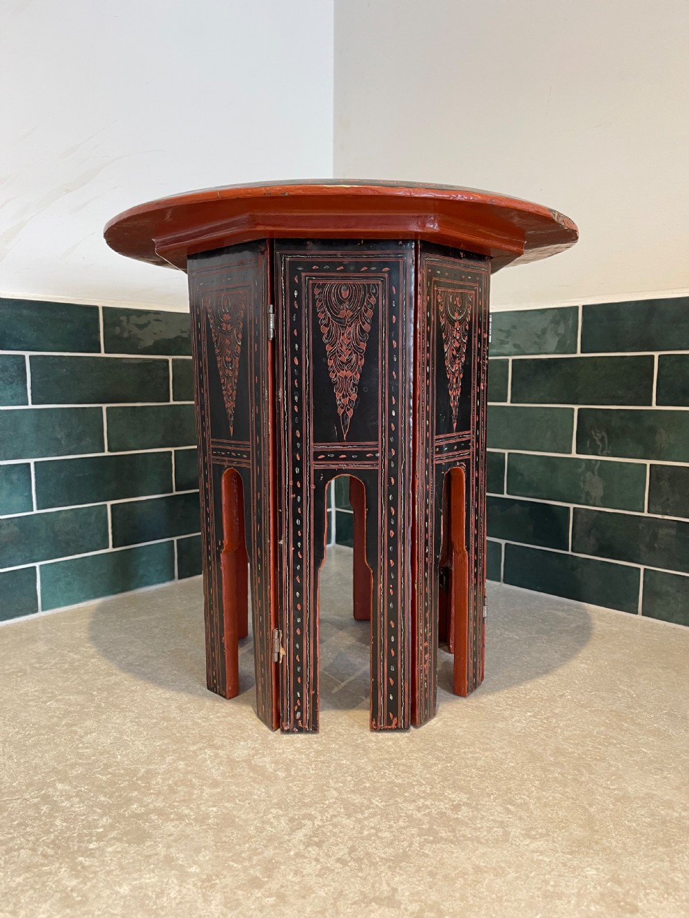 An octagonal Burmese lacquered folding side table featuring black and red panels decorated with incised geometric and floral motifs above arched openwork legs.